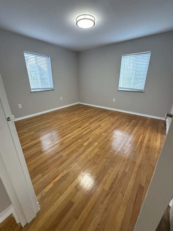 A room with wooden flooring and two windows.
