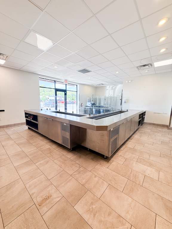 A large, empty kitchen with a tile floor and a large island in the middle.