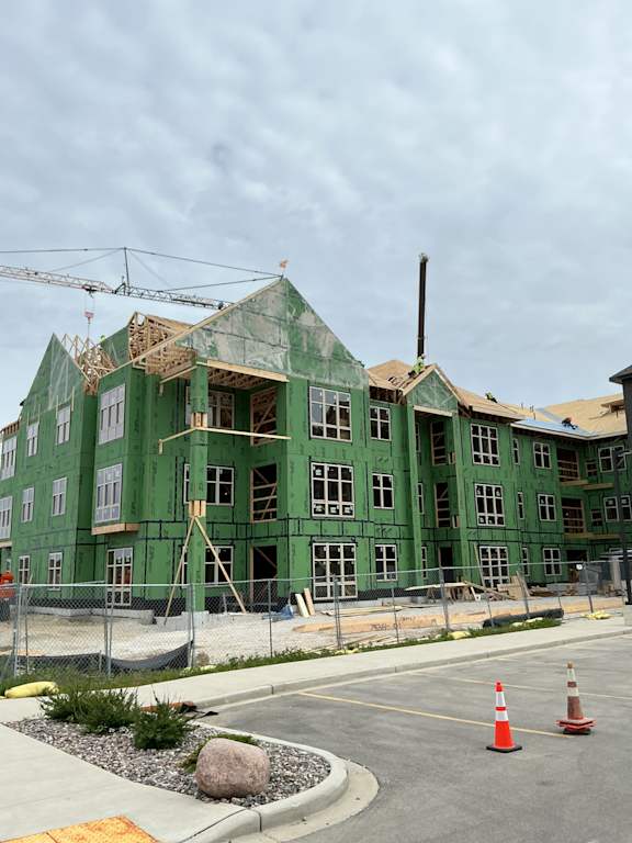 A green building under construction with a crane in the background.