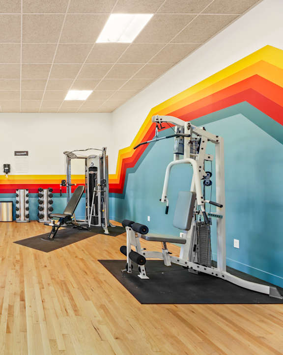 A gym with a variety of equipment including a bench press, a squat rack, and a leg press machine.