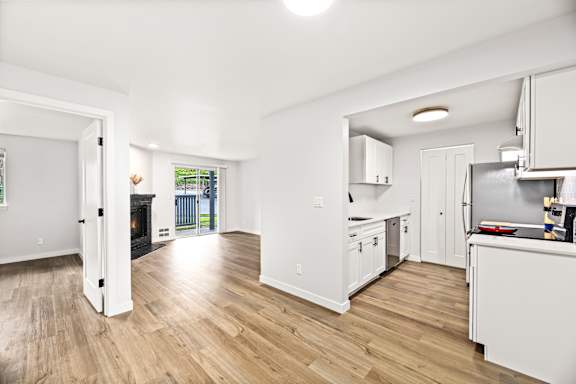 the living room and kitchen of a house with white walls and wooden floors