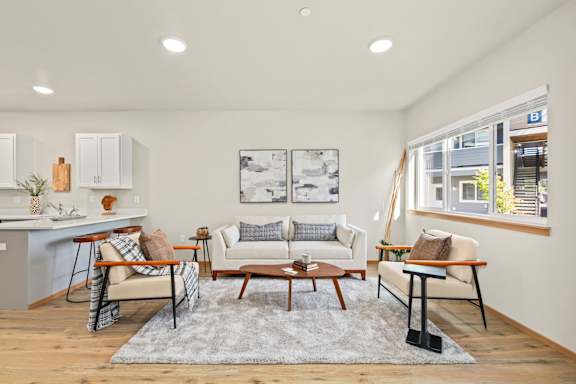 a living room with couches and chairs and a kitchen with a staircase