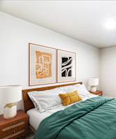 A bedroom with a bed, two lamps, a potted plant, and two framed pictures on the wall.