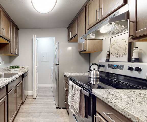 A kitchen with gray granite countertops, wood cabinets, and stainless-steel appliances at A'Cappella.