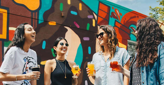 Four women are standing in front of a colorful wall.