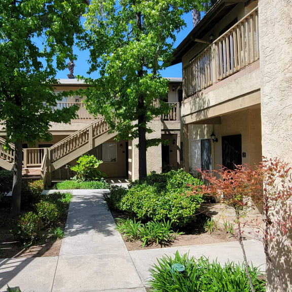 a walkway between two apartment buildings with trees and bushes