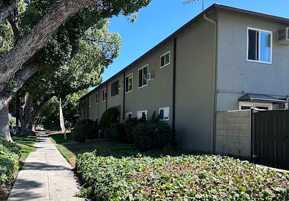 a gray apartment building with a sidewalk and trees in front of it