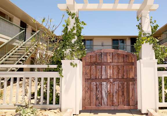 a wooden gate in front of a house with a white pergola