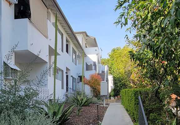 A white building with a balcony is surrounded by green plants.