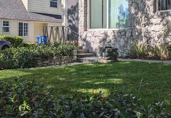 a yard with green grass and a stone house in the background