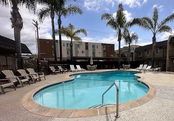 a swimming pool with lounge chairs and palm trees in the background