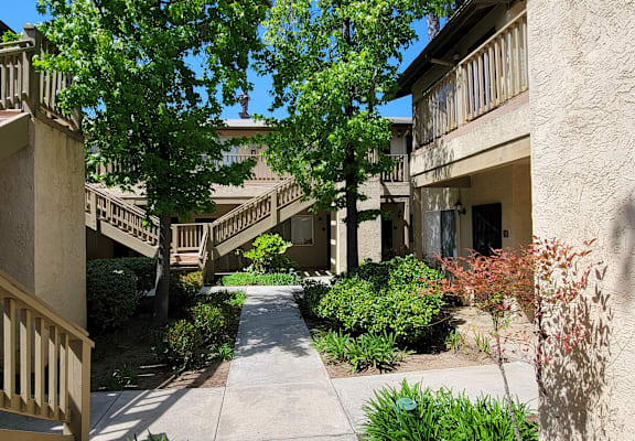 a walkway between two apartment buildings with trees and bushes