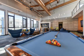 Community Clubhouse Pool Table with Blue Chairs, Brown Sofa and Hanging Ceiling Lights
