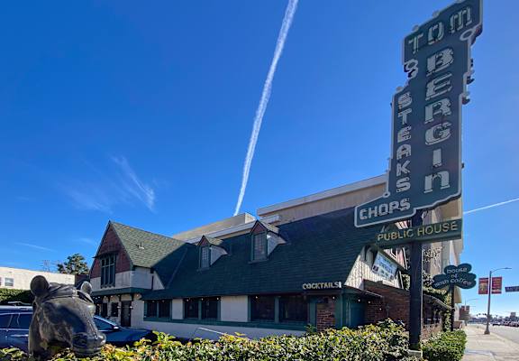 A restaurant named Toms Burgers has a green awning and a sign with a rhino head on it.