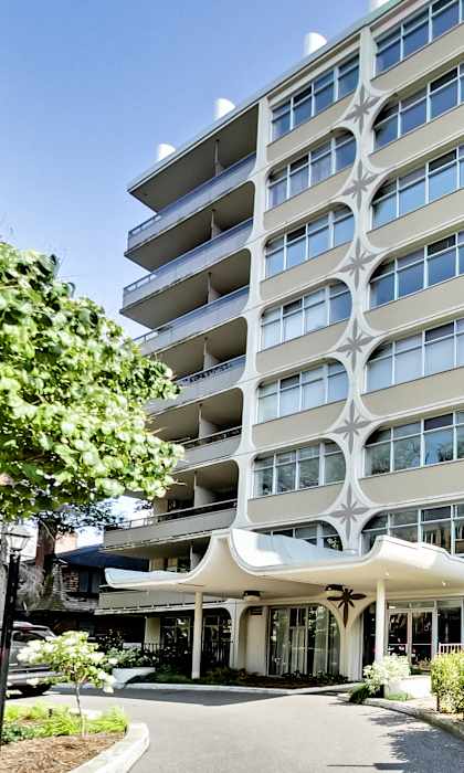 A large white apartment building with balconies and a covered walkway.