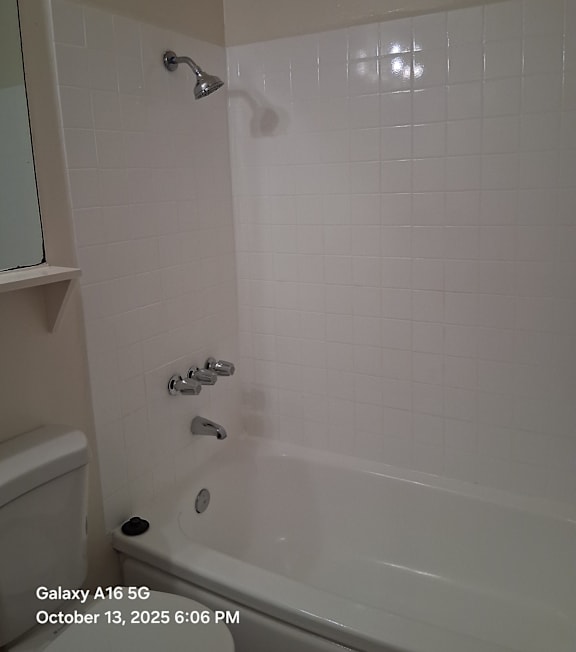 A white tiled bathroom with a shower and a toilet.