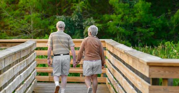 Two elderly people walking on a wooden bridge.