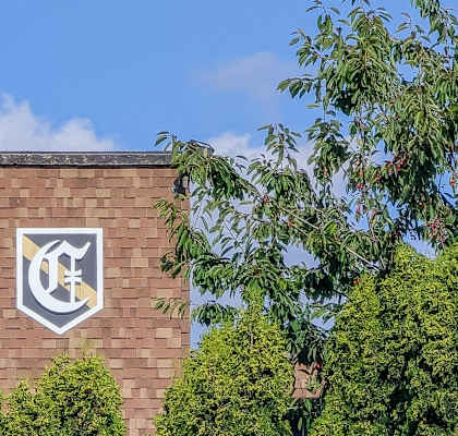 A building with a white emblem on a brick wall surrounded by greenery.