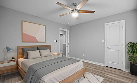 A bedroom with a bed, a ceiling fan, and a painting on the wall.