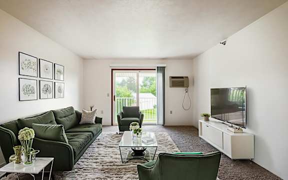 A living room with a green couch, a glass coffee table, and a flat screen TV.