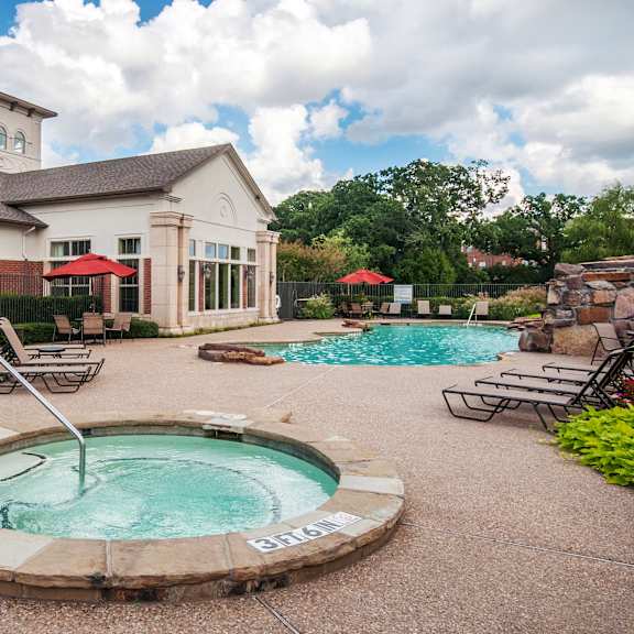 The fun hot tub at the Landing at Mansfield Apartments with chairs, the turquoise pool, and the white clubhouse in the background.