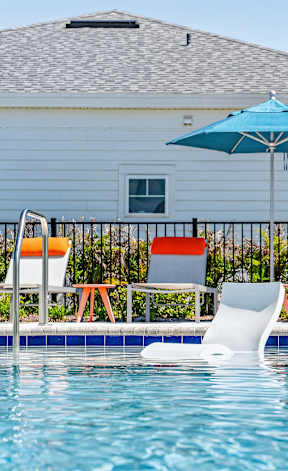 A pool with chairs and an umbrella in front of a house.