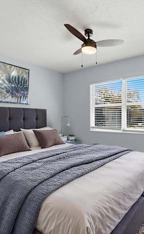 A bedroom with a bed, a ceiling fan, and a potted plant.