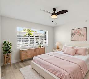 A bedroom with a pink bedspread and a ceiling fan.