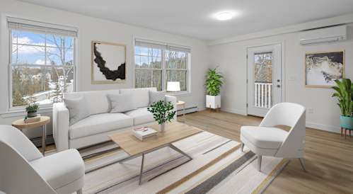 A living room with a white couch, a coffee table, and a large window with a view of the outdoors.