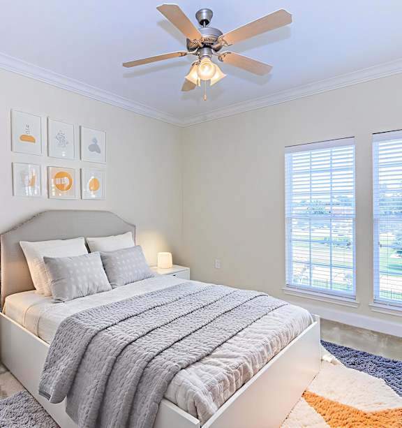 A bedroom with a bed, a ceiling fan, and pictures on the wall.
