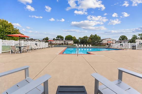 A pool surrounded by a white fence and a red umbrella.