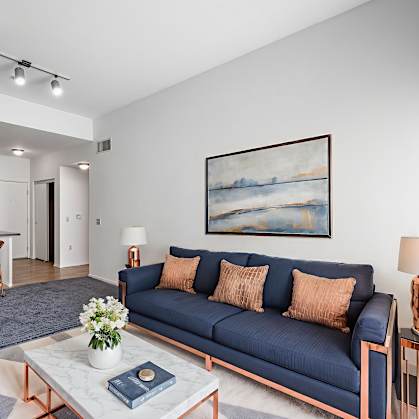A living room with a blue couch and a painting on the wall.