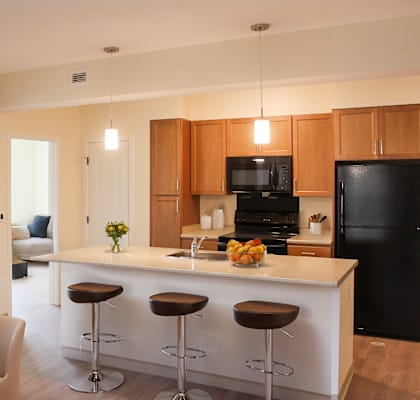 A kitchen with a black refrigerator, wooden cabinets, and a white island.