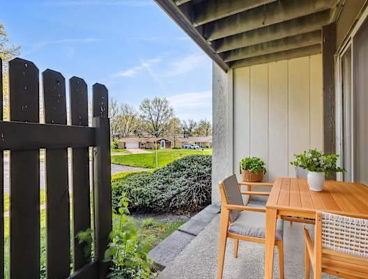 A wooden table and chairs are on a patio with a view of a backyard.