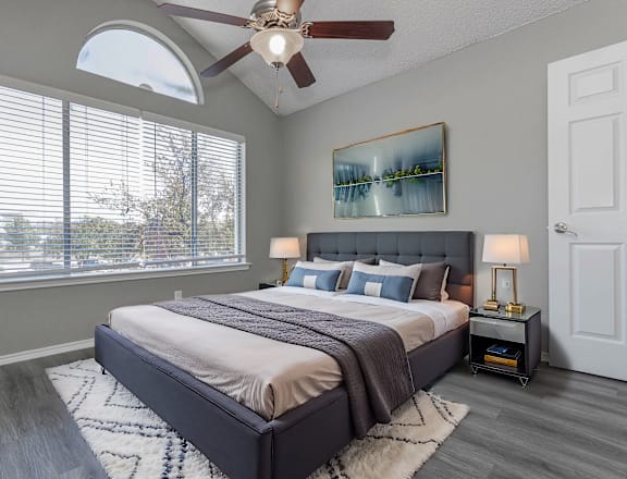 A bedroom with a large bed, a ceiling fan, and a painting on the wall.