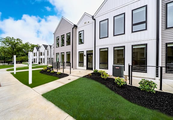 A row of modern houses with white fences and green lawns.