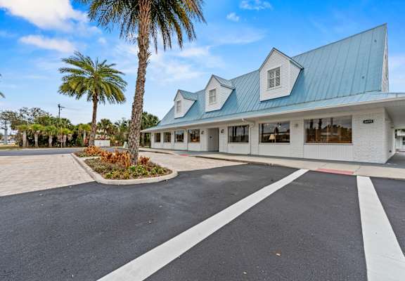 A white building with a blue roof and a palm tree in front.at The Teale New Haven Apartments, Melbourne, FL, 32904