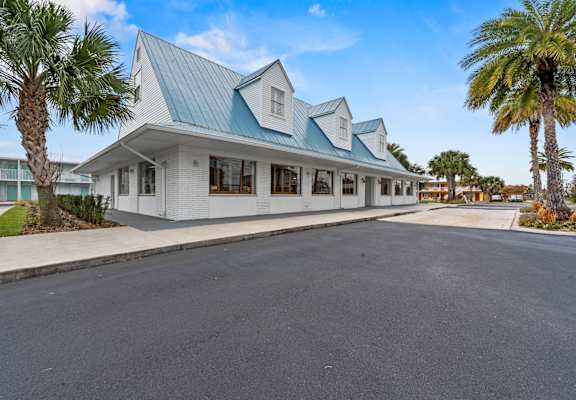 A white building with a blue roof is surrounded by palm trees.at The Teale New Haven Apartments, Melbourne, FL, 32904