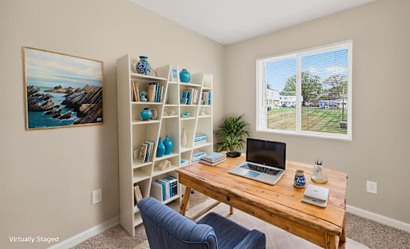 A room with a bookshelf, a laptop, and a painting on the wall.