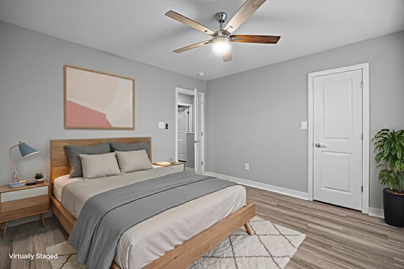 A bedroom with a bed, a ceiling fan, and a painting on the wall.