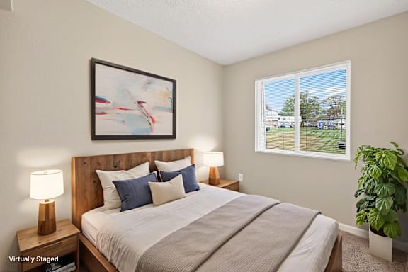 A bedroom with a large bed, a lamp, a painting, and a potted plant.