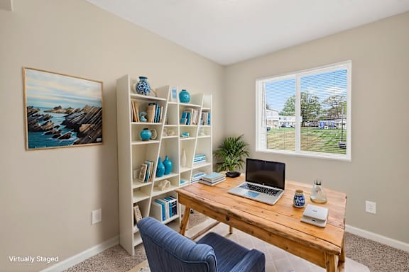 A room with a bookshelf, a laptop, and a painting on the wall.