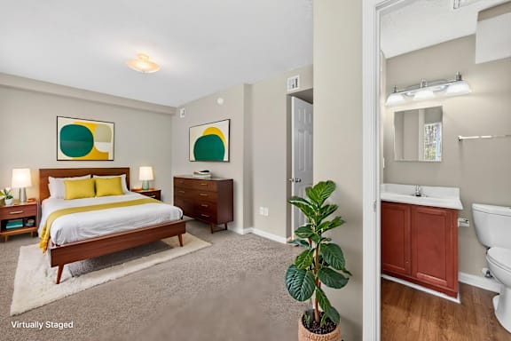 A bedroom with a bed, nightstand, and a plant.