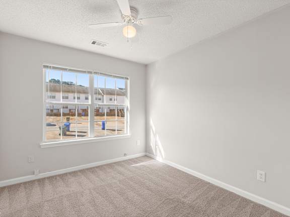 A room with a carpeted floor, a ceiling fan, and a window showing an outdoor view.