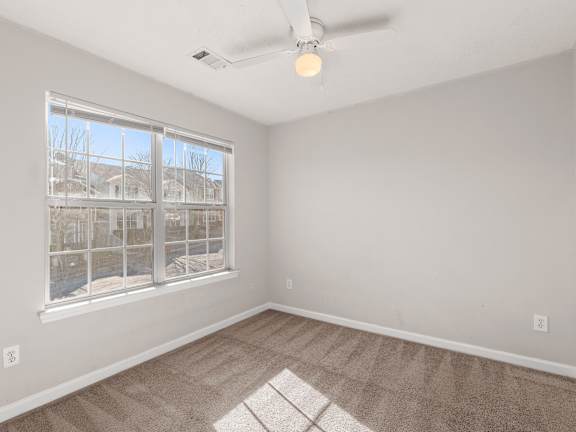 A room with a carpeted floor, a ceiling fan, and a large window.