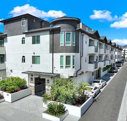 A row of modern townhouses with white and grey exteriors and green plants in front.