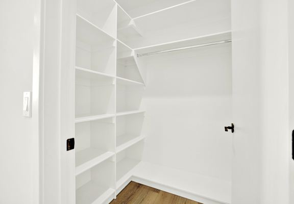 A white shelving unit in a room with a light switch on the wall.
