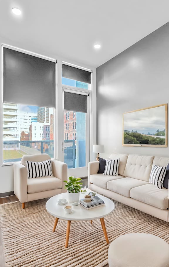 A living room with a white sofa, a coffee table, and a large window with a view of the city.