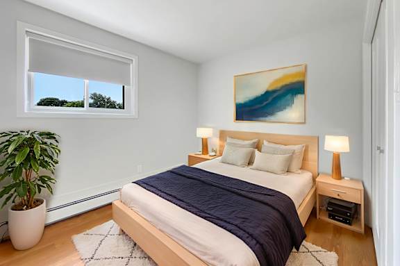 A bedroom with a bed, nightstand, and a painting on the wall.