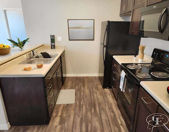 A kitchen with a black fridge and wooden floors.